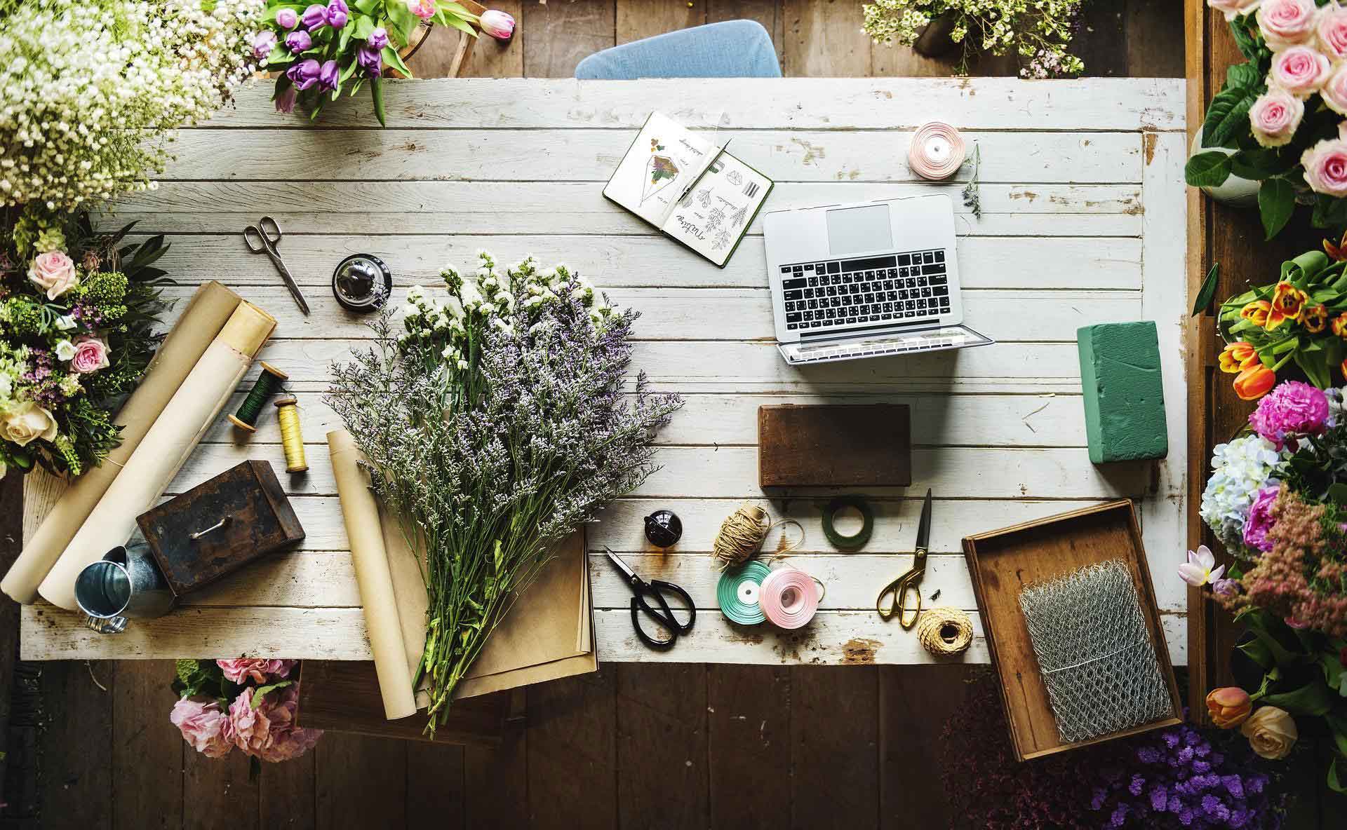 Aufsicht auf Gartentisch mit Laptop und Blumenbinden-Zubehör