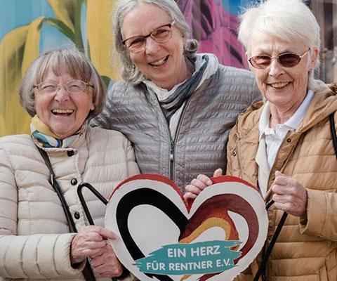 Drei Seniorinnen stehen vor dem Firmenschild von EIN HERZ FÜR RENTNER e.V.