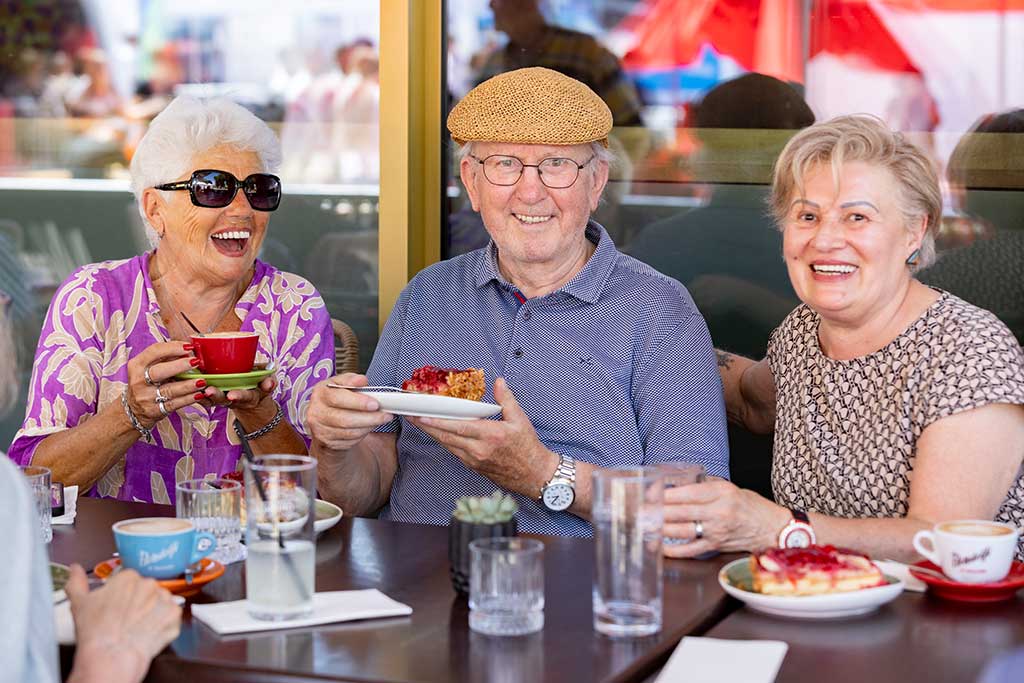 Drei Senioren sitzen lachend in einem Cafe und essen Torte